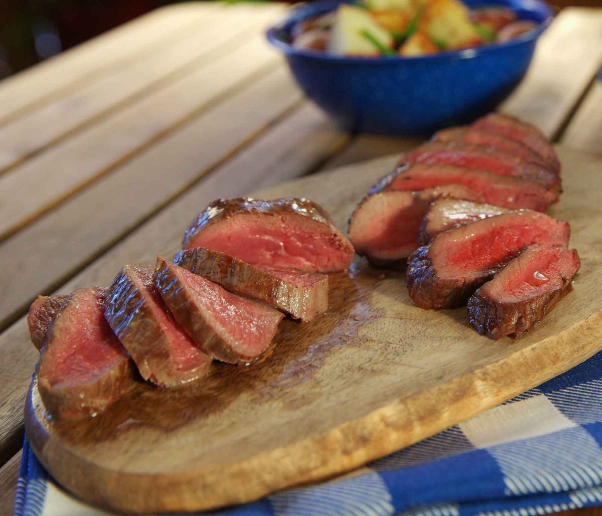 Juicy bourbon marinated elk steaks on a wooden tray.