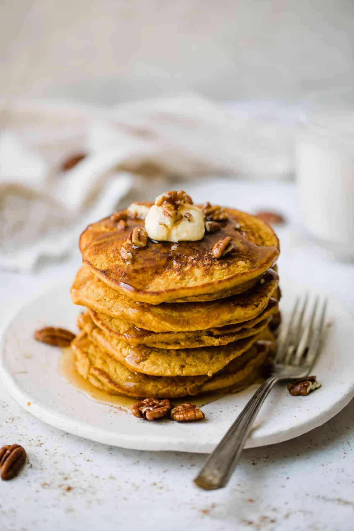 A pile of healthy pumpkin oatmeal pancakes on a plate with a fork.